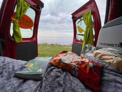 View of the ocean steps away from the opened back doors of a small VW campervan at a campsite along the northern coast of Iceland